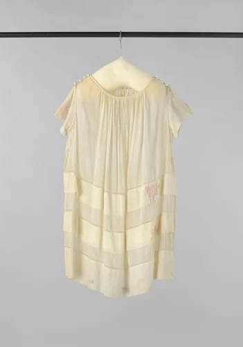 Kinderjurk met korte mouw, plooien vanuit de hals en vier gehaakte bollen op de schouder van wit katoen, versierd net ajourranden en twee stroken met roze geborduurde bloemen by anonymous, other, 1900-1925