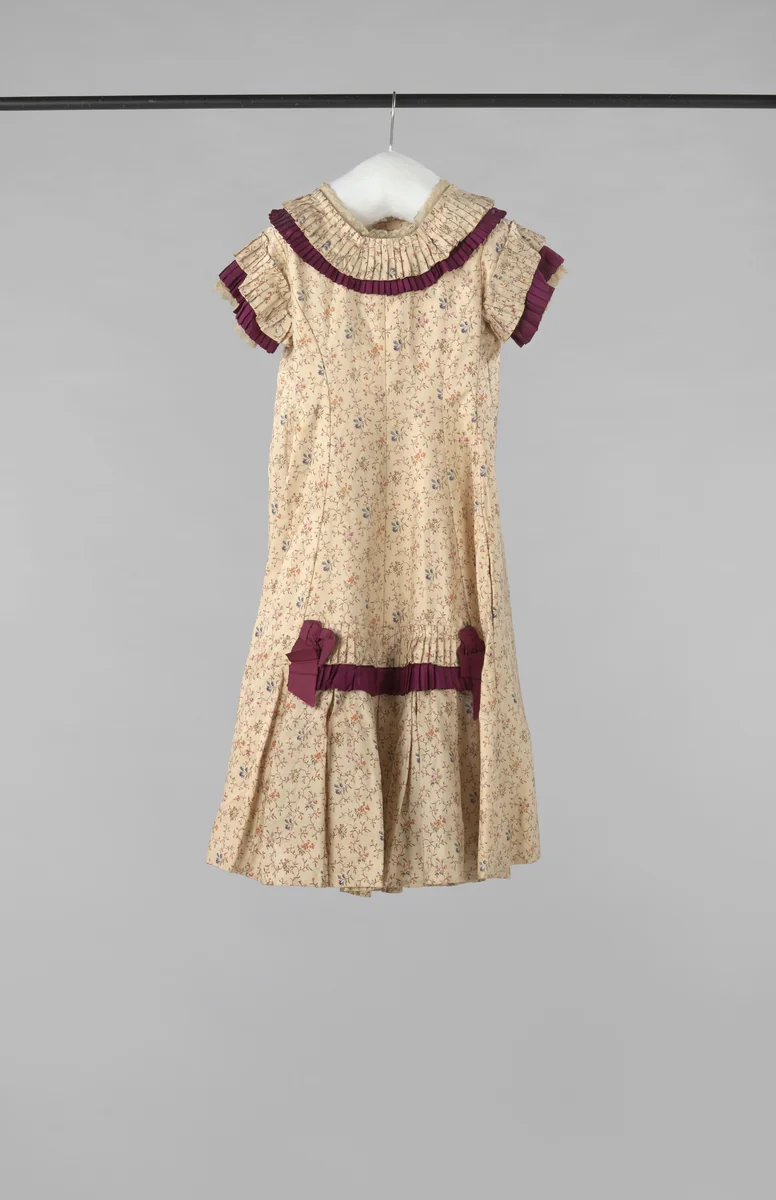 Een feestjurkje van bedrukte creme zijde met bloemtakjes, opgemaakt met karmijnrode strikjes en stroken by anonymous, other, 1880-1885