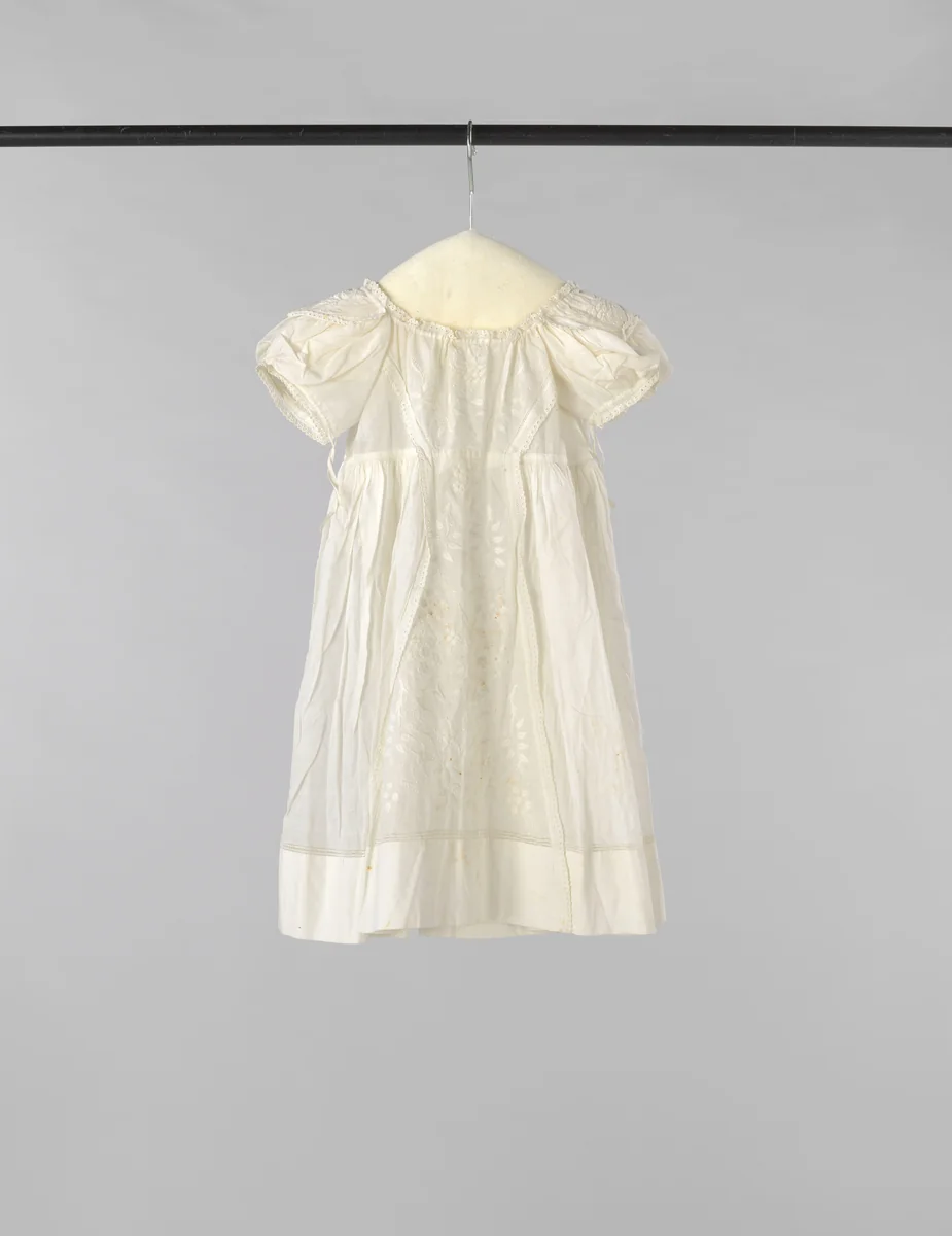 Kinderjurk met hoge taille en achtersluiting met striklinten van witte batist, voor versierd met een breed tussenzetsel plumetis en op de korte pofmouw ook met plumetis. by anonymous, other, 1850-1900
