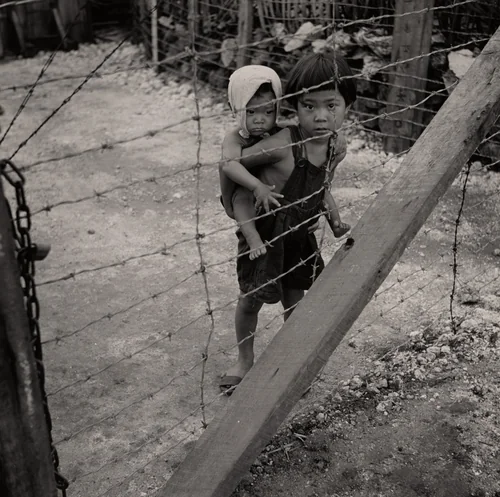Child with Infant on His Back behind Barbed Wire. Prison for Suspected Collaborators, Guam by Wayne Miller, photograph, 1944
