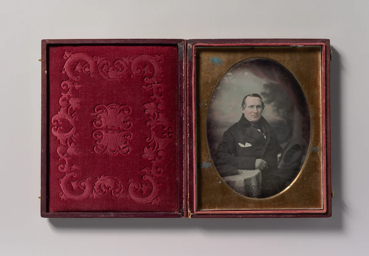 [Man Wearing Coat and Gloves, Holding Hat, Seated in Front of Painted Outdoor Backdrop] by Samuel Broadbent Jr., photograph, 1840-1849