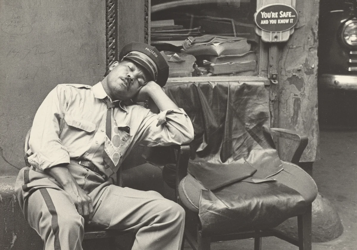 At the same time Mel, his morning duties done, has changed his uniform and rests in one of the garage chairs. by Robert Frank, photograph, 1951