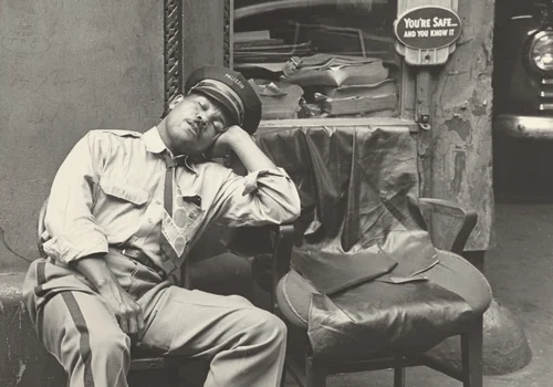 At the same time Mel, his morning duties done, has changed his uniform and rests in one of the garage chairs. by Robert Frank, photograph, 1951