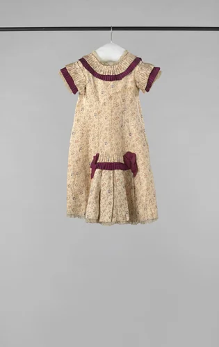 Een feestjurkje van bedrukte creme zijde met bloemtakjes, opgemaakt met karmijnrode strikjes en stroken. Het schootje is van glasbatist, en onder de rokzoom komt een Valenciennes-kant te voorschijn by anonymous, other, 1880-1885