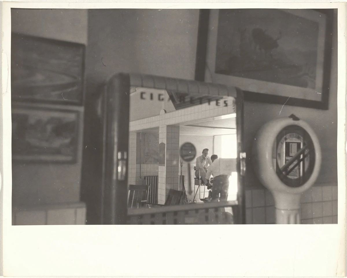 Shining shoes, reflection in cigarette machine mirror--New Mexico by Robert Frank, photograph, 1955