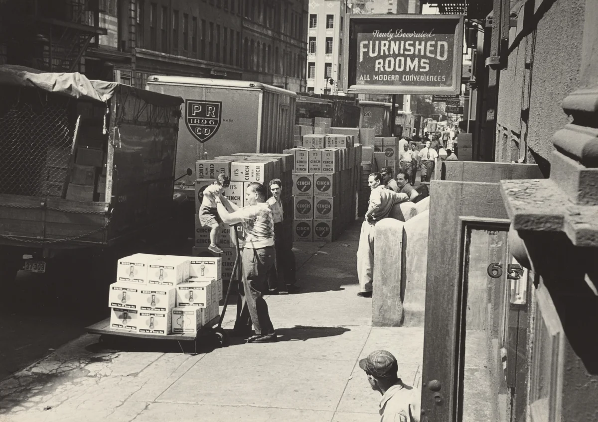 By 10 o'clock Georgie has been sent out of the rooming house to his playground--the sidewalk. His friends, truckmen and loaders, keep an eye on him during the day. by Robert Frank, photograph, 1951