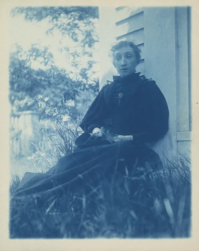 Untitled (Woman seated against a clapboard building) by American 20th Century, photograph, 1890-1910