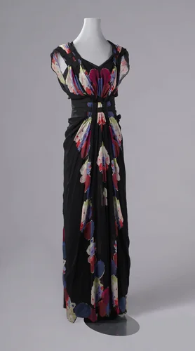 Rok van een avondjapon in smal model van zwarte crêpe, met een baan aan de rechterkant van kleurige bloemen, op sommige plekken opgefestonneerd; achter 13 stofknoopjes by Nina Ricci, textile, 1938