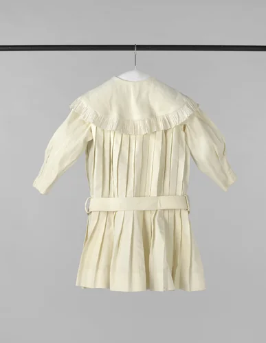 Een kleuterjurk van in plooien genaaide piqué, voorzien van ronde liggende kraag met batisten ruches en een stoffen ceintuur by anonymous, other, 1875-1880