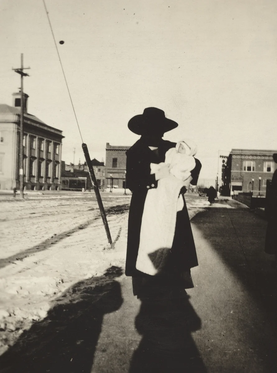 Untitled (Woman holding baby on street) by American 20th Century, photograph, 1890-1919