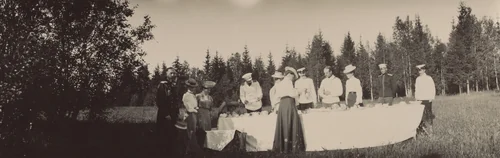 Grand Dukes Alexander Mikhailovich and Michael Alexandrovich, and Grand Duchess Xenia Alexandrovna, with Others, Standing Around a Table, Gatchino, by Unidentified Photographer, photograph, 1905